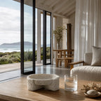 Textured concrete bowl with irregular form on wooden table in coastal living room featuring ocean view.