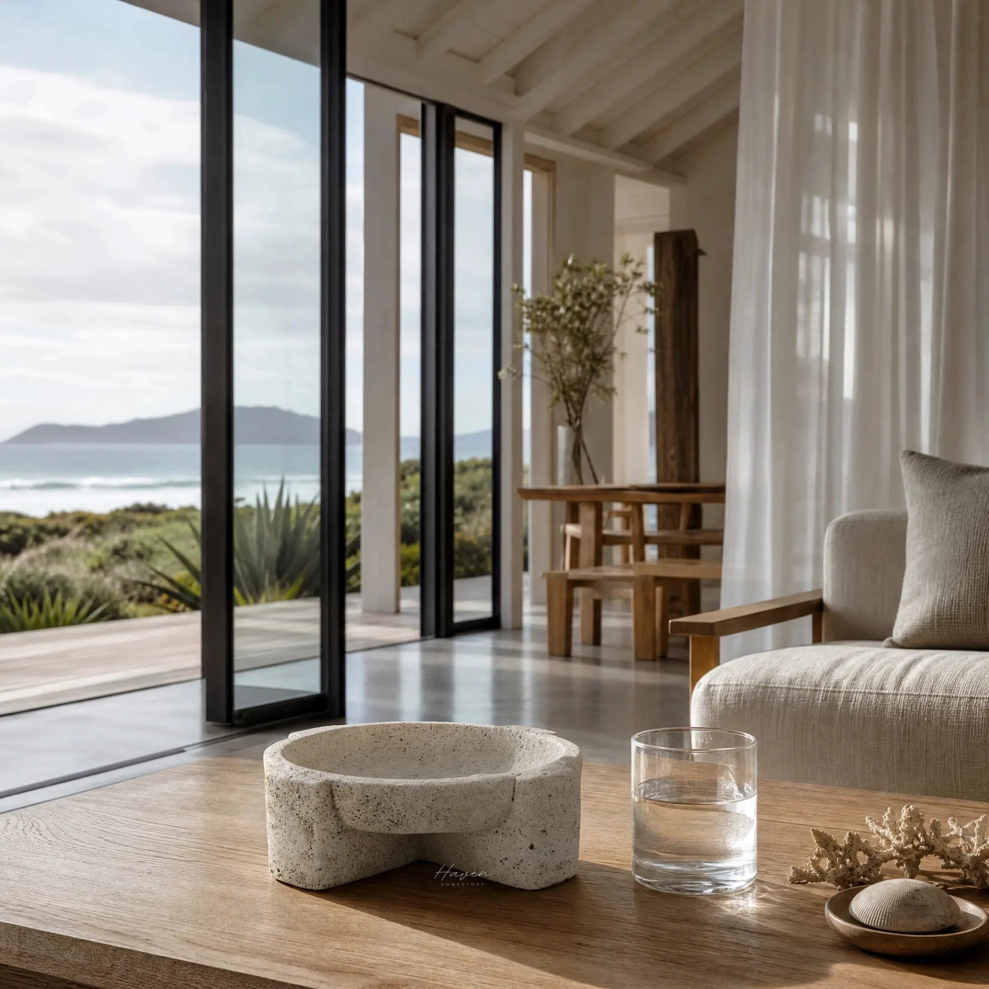 Textured concrete bowl with irregular form on wooden table in coastal living room featuring ocean view.