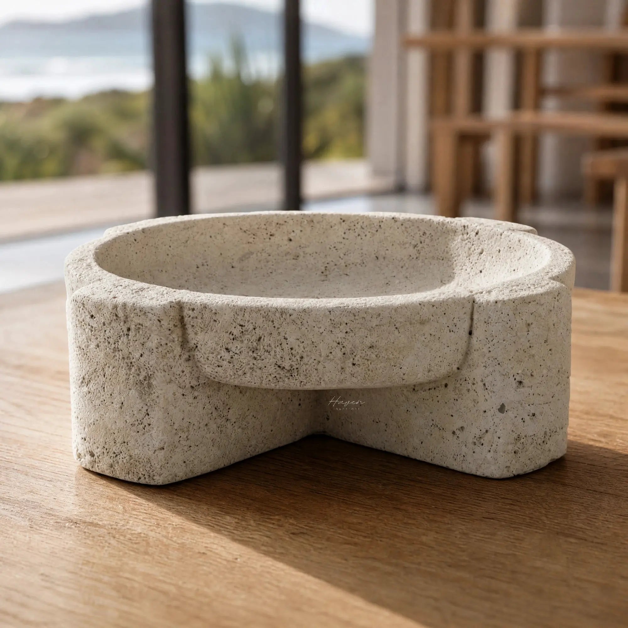 Textured concrete bowl with sculptural, irregular form and weathered stone finish resting on a wooden table.
