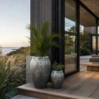 Textured black-grey fibre cement lava planters set displaying rounded forms on a wooden deck beside modern architecture and ocean view.