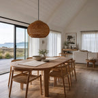 Banana leaf pendant light with teak top detail hanging above a wooden dining table in a bright coastal room.