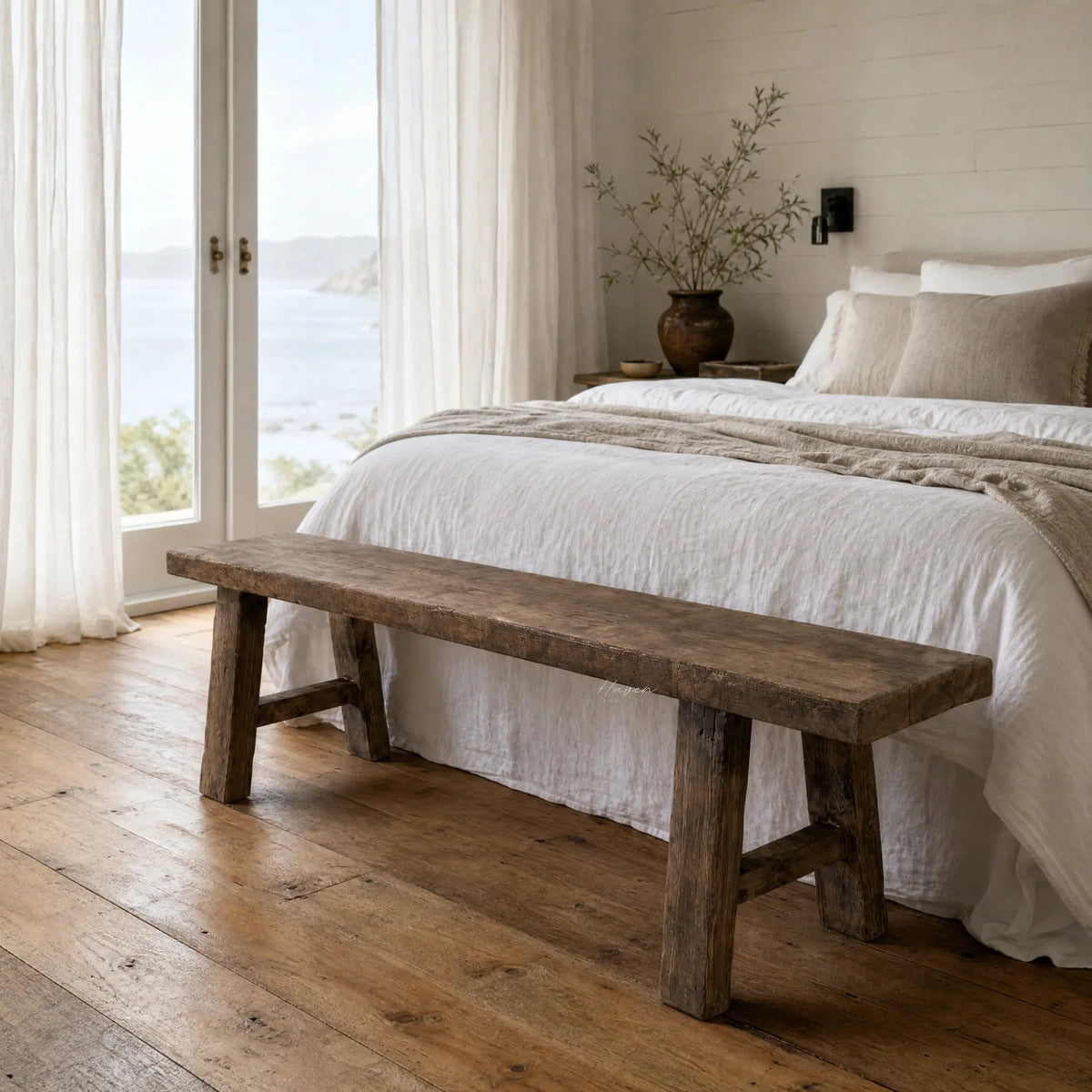 Rustic reclaimed elm bench with substantial legs at the foot of a bed, featuring visible knots and grain.