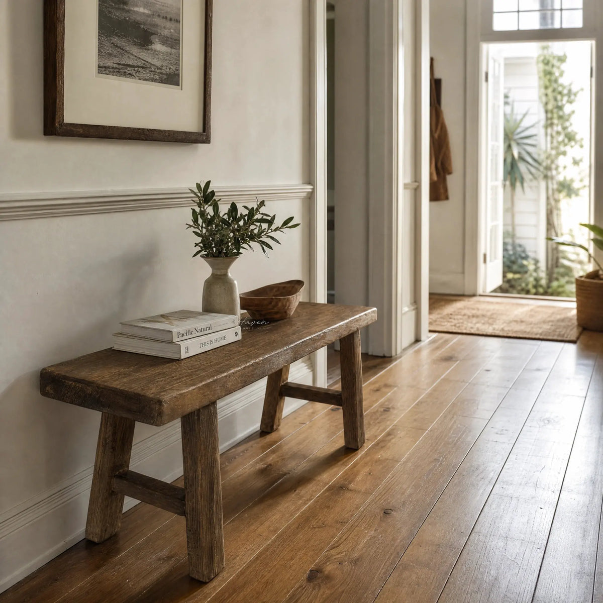 Rustic reclaimed elm bench with broad seat and substantial legs, featuring visible grain and knots in a sunlit hallway.