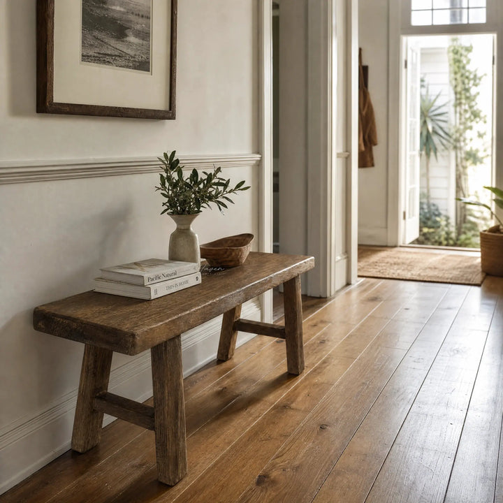 Rustic reclaimed elm bench with broad seat and substantial legs, featuring visible grain and knots in a sunlit hallway.