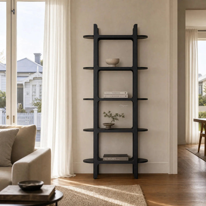 Tall black architectural bookcase with rounded corners and shelves extending beyond vertical supports, styled with books and decor in a bright living room.