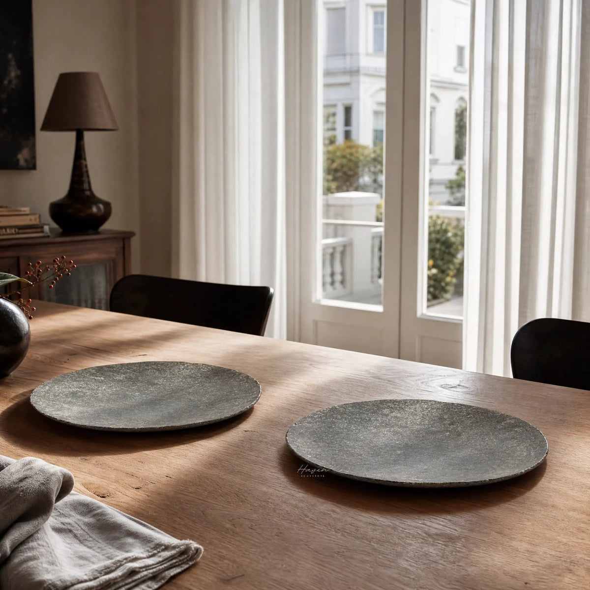 Two dark grey rectangular riverstone plates with irregular edges and sculptural texture on a wooden dining table.