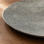 Close-up of a textured grey riverstone plate with an irregular sculptural edge resting on a wooden surface.