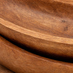 Close-up of solid teak oval trays featuring gently upturned edges, warm brown tones, and visible natural wood grain texture.