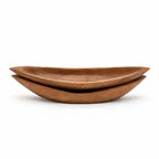Stacked oval teak trays with warm brown tones, visible grain, and gently upturned edges carved from solid wood.