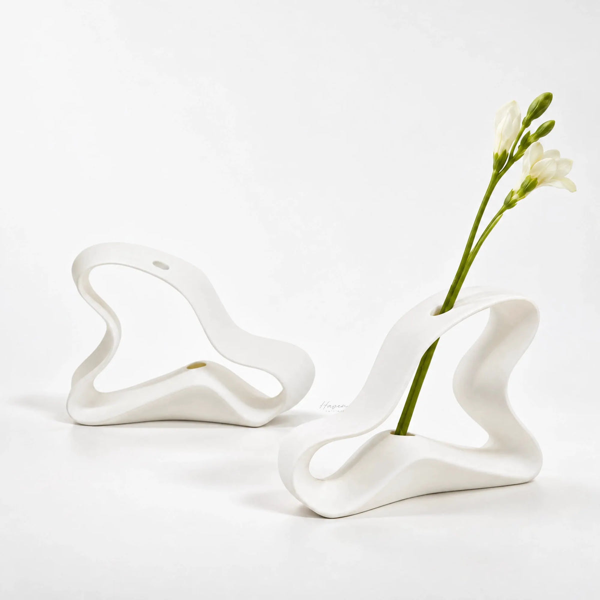 Set of two white bone china bud vases featuring a sculptural, ribbon-like silhouette with fluid curves and open negative space.