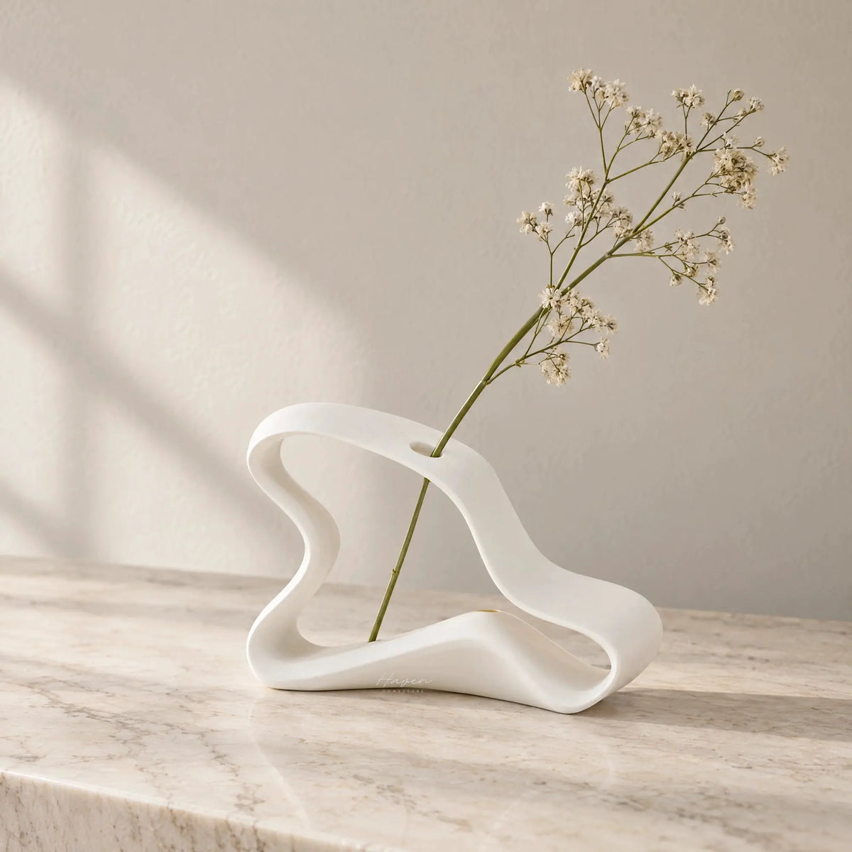 White bone china Infinity Ribbon bud vase with sculptural ribbon silhouette holding baby's breath on marble.