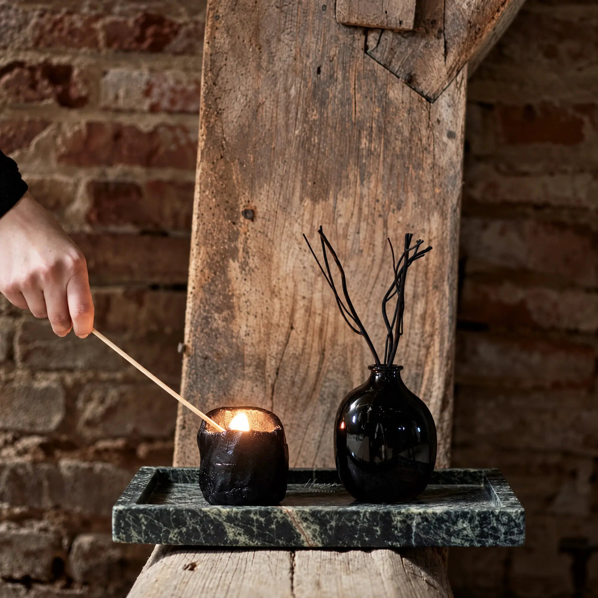 Green marble tray with low profile holding a black candle and vase on rustic wood beam.