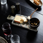 Green marble serving board with integrated handle displays cheese, capers, and dip on a dark wooden table setting.
