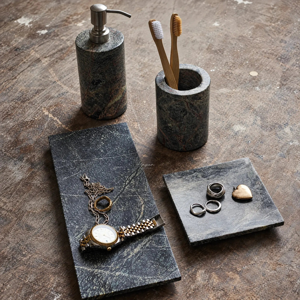Long and square green marble trays holding jewelry, paired with a soap dispenser and toothbrush holder on a rustic surface.