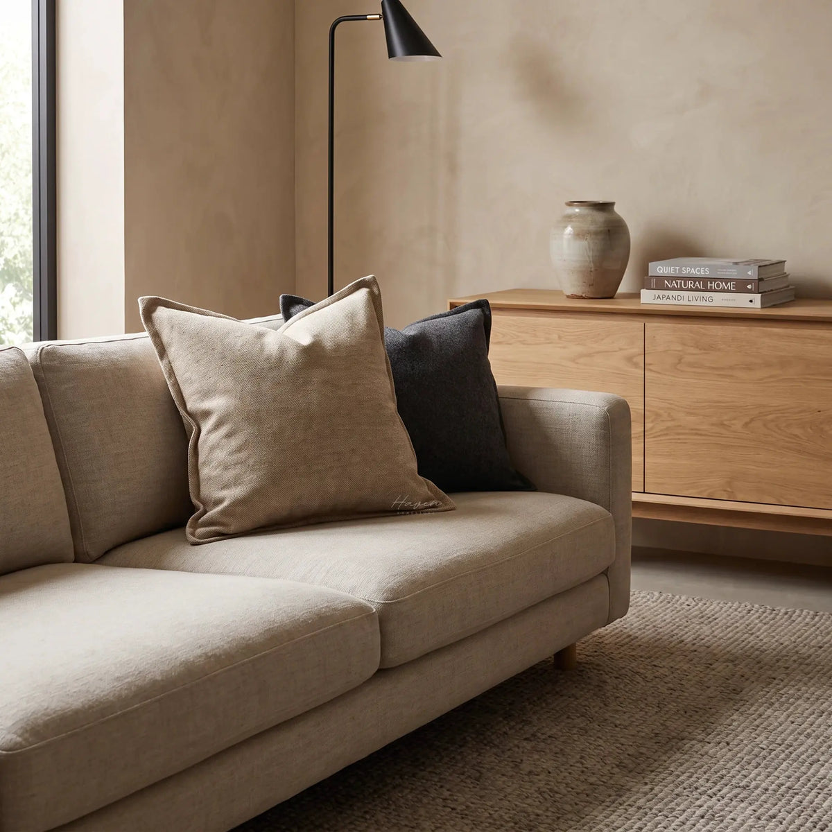 Textured oat cushion cover on a beige sofa, featuring a woven surface and relaxed scale in a warm living room.