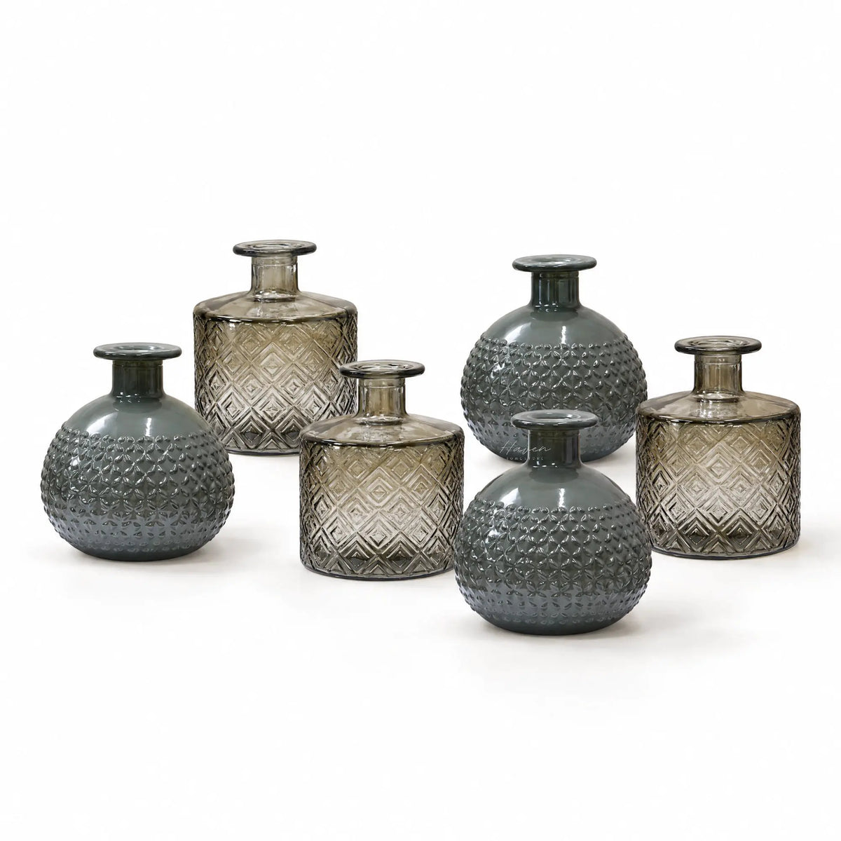 Set of six smoked glass bottles with embossed geometric textures, featuring alternating round and cylindrical shapes in soft grey tones.