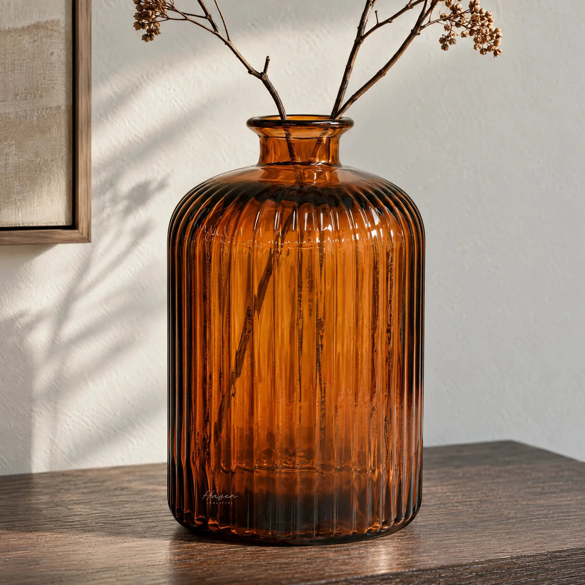 Amber glass vase with vertical fluting and rounded shoulders holding dried branches on a wooden surface.