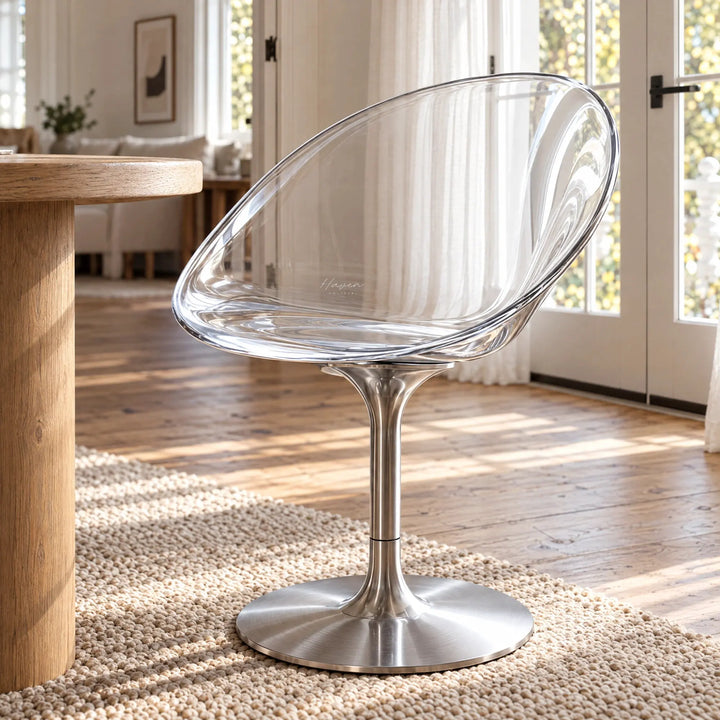 Clear polycarbonate swivel chair with curved transparent shell and slender silver aluminium pedestal base on a textured rug.