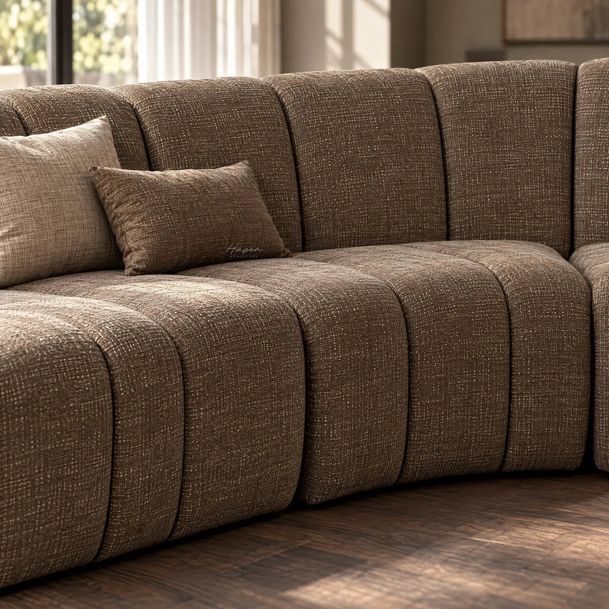 Curved modular sofa in textured truffle polyester. Features softly segmented design, low back, and matching cushions for a relaxed architectural look.