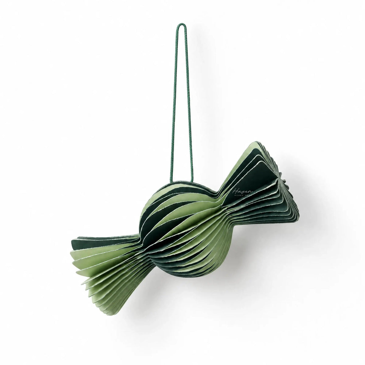 Layered paper candy ornament in alternating light and forest green folds, creating a sculptural ribbed texture with a matching green hanging cord.