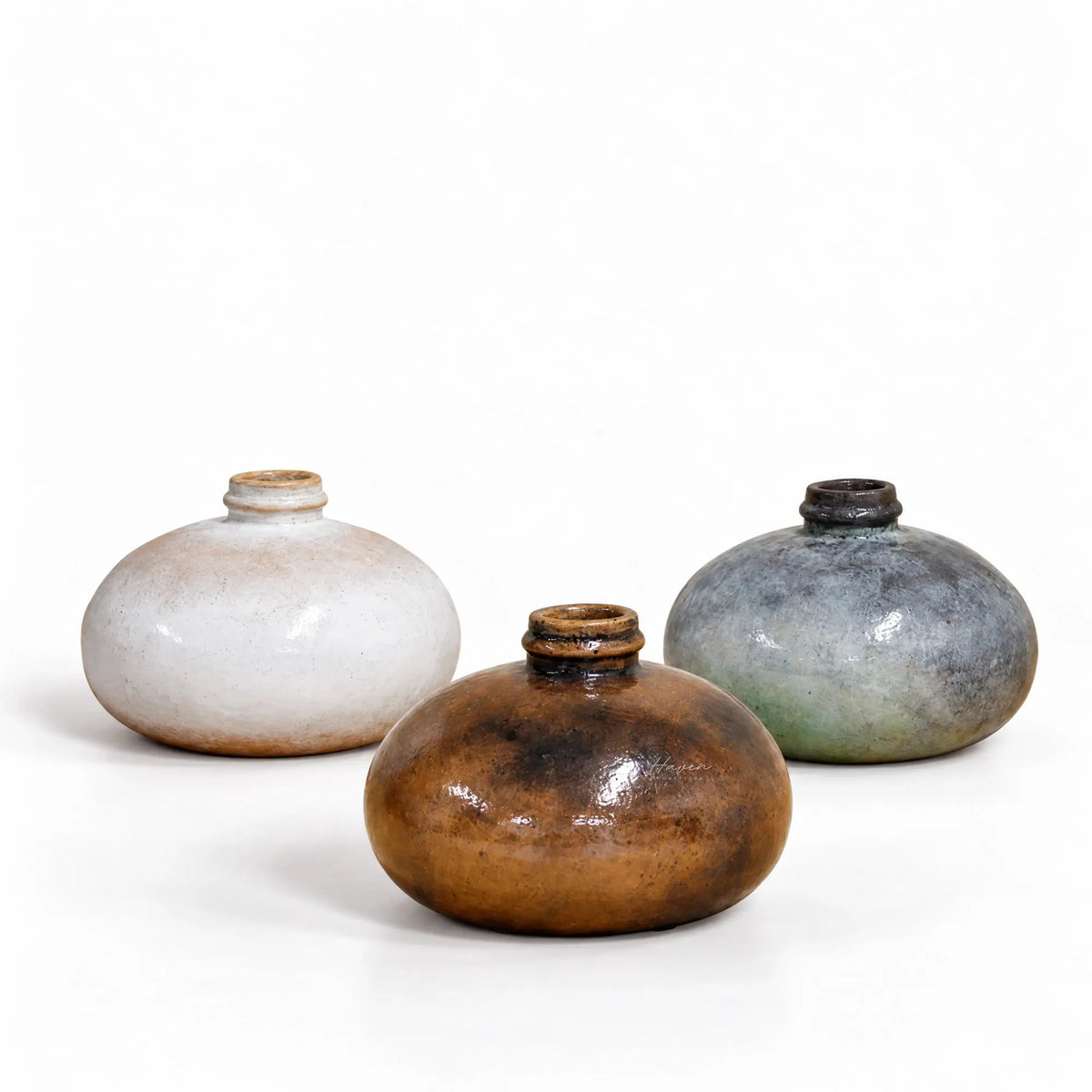 Set of three hand-thrown low round ceramic vessels with glossy earthy glazes in cream, brown, and slate blue.
