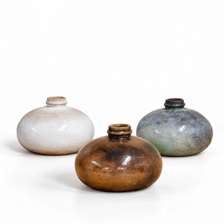 Set of three hand-thrown low round ceramic vessels with glossy earthy glazes in cream, brown, and slate blue.