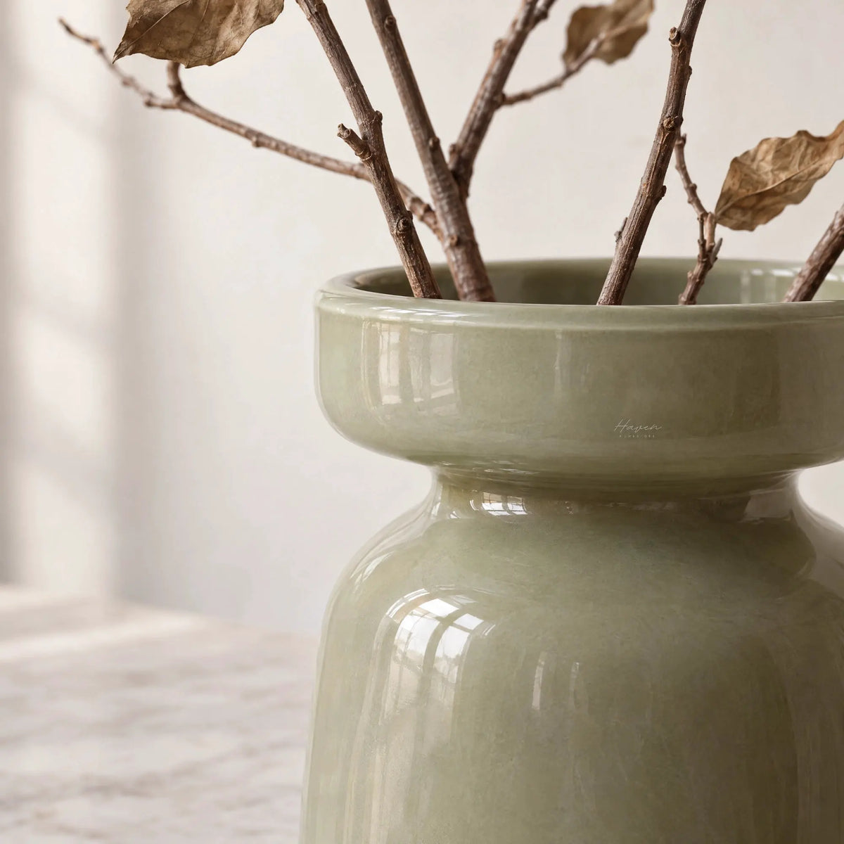 Light green mouthblown glass vase with softly rounded silhouette and flared rim, holding dried branches.