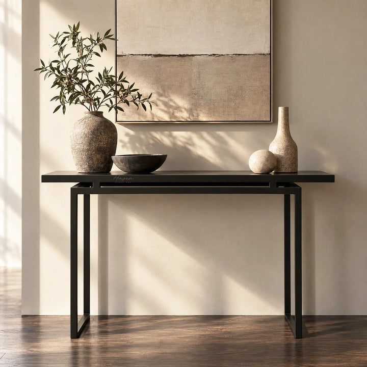 Slim metal console table in greyed-brown with an architectural frame, styled with ceramic vases and greenery against a neutral wall.