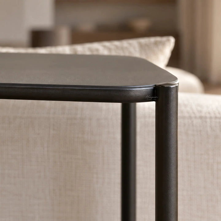 Greyed-brown low profile shelf with slim metal construction and rounded corner detail, offering a quiet architectural presence beside a sofa.