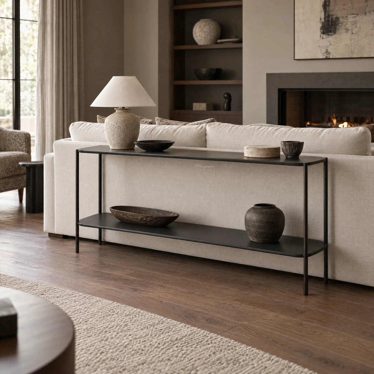 Long, slim two-tier metal shelf in greyed-brown placed behind a sofa, featuring a low profile and open design for decorative display.