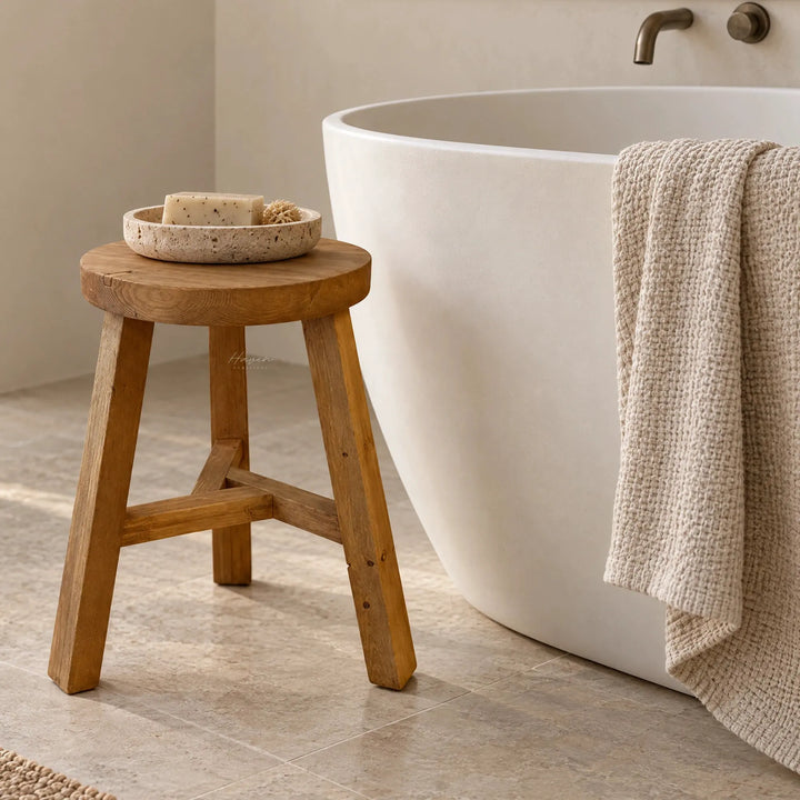 Compact reclaimed elm stool with visible knots and grain standing beside a white freestanding bathtub holding a stone soap dish.