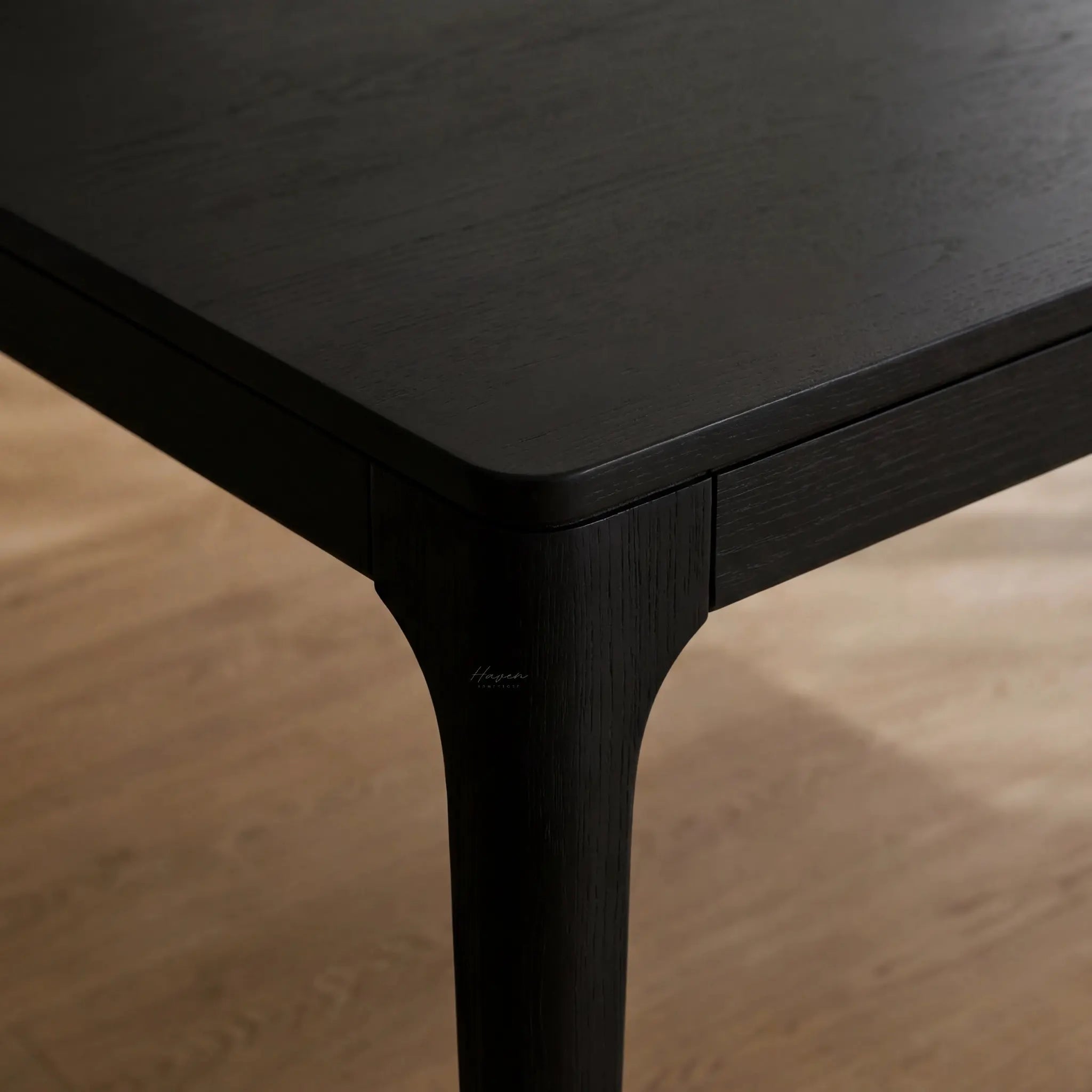 Close-up of the black Baur Dining Table corner and leg, highlighting the ash wood grain.