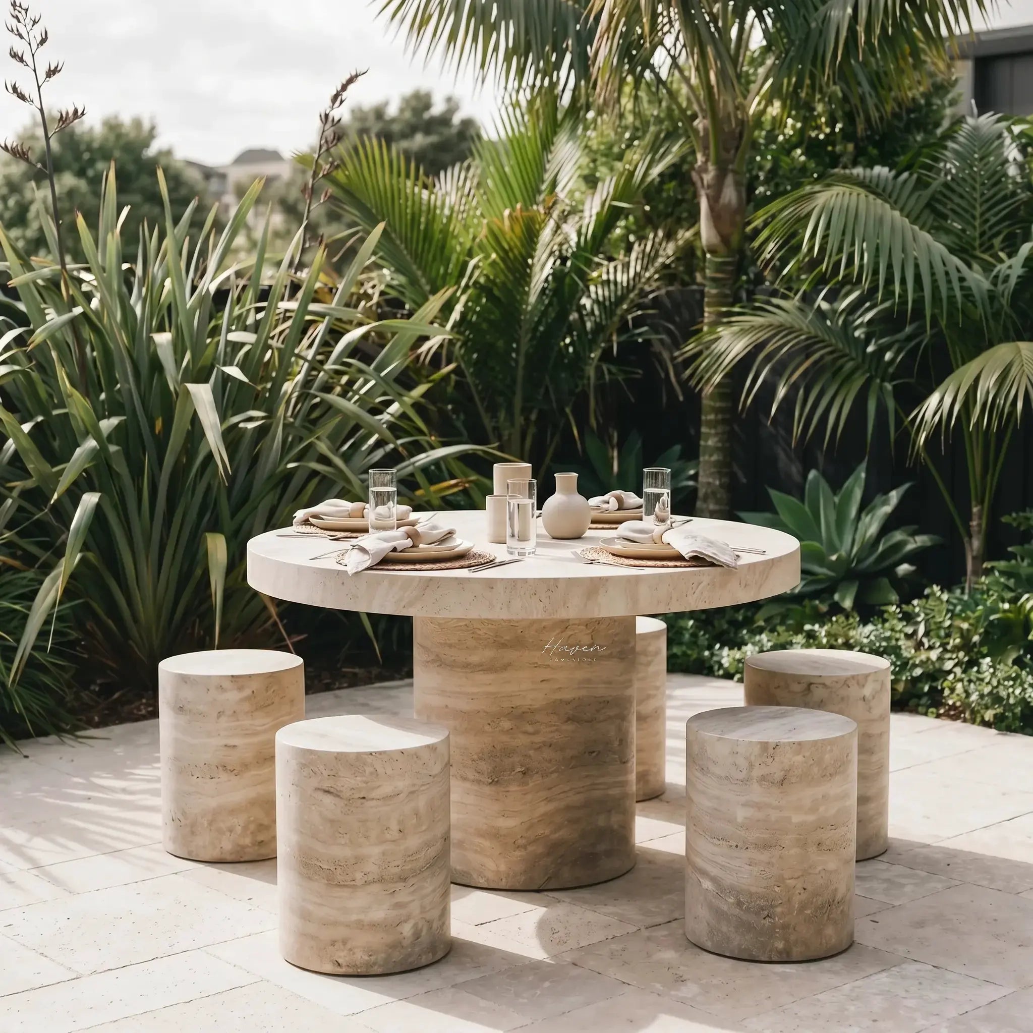 Tivoli Travertine Dining Table with round travertine top and sculptural pedestal, outdoor dining amid tropical plants.