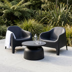 Eden Chair outdoor lounge in dark gray polypropylene beside a round table with a water bottle, lush garden backdrop