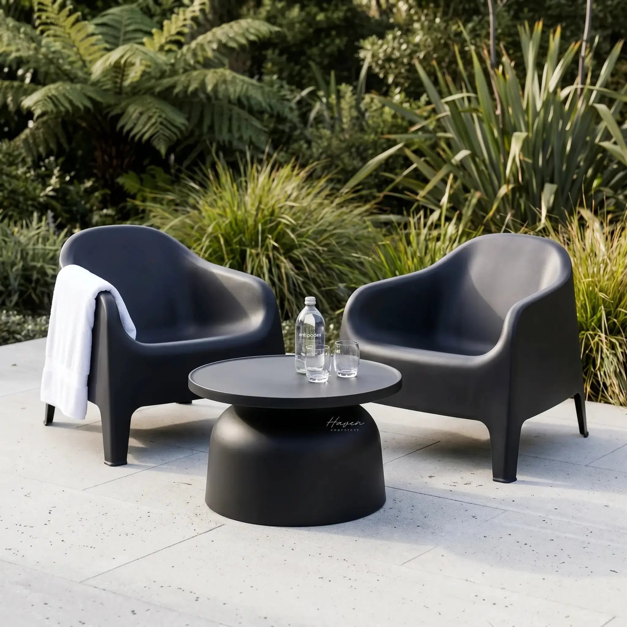 Eden Chair outdoor lounge in dark gray polypropylene beside a round table with a water bottle, lush garden backdrop