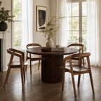 Dune Teak Dining Chair around a round teak table in a sunlit dining room with white curtains.