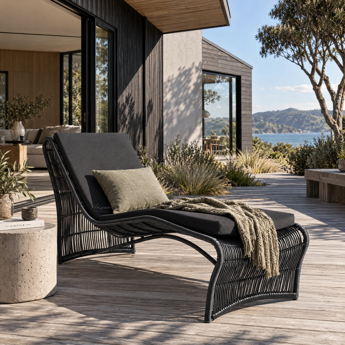 Sculptural black wave sun lounger with curved aluminium frame and woven synthetic fibres on a wooden deck overlooking the ocean.