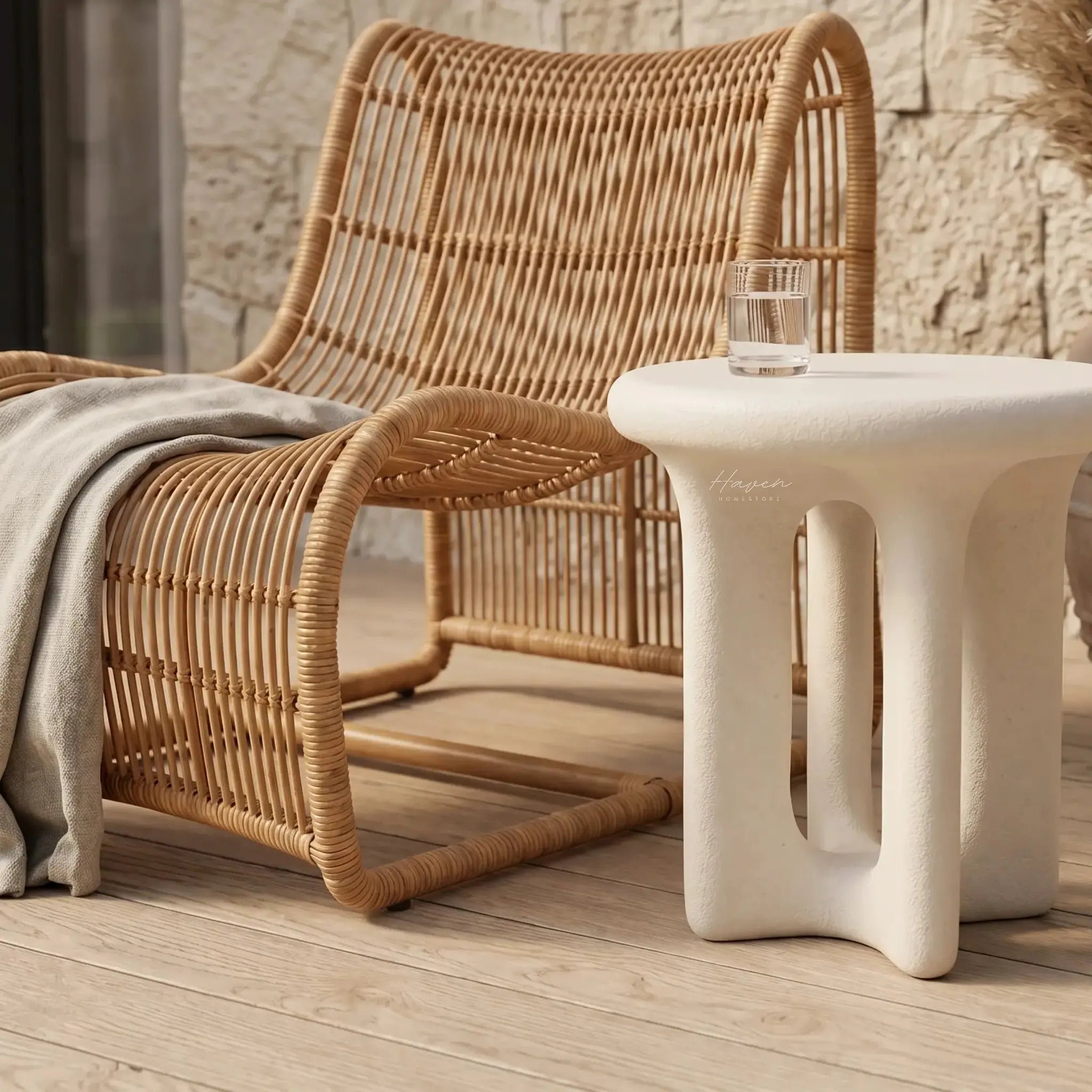 Yepa End Table with sculptural curves and linen-toned GRC, stone-like texture beside a wicker chair.