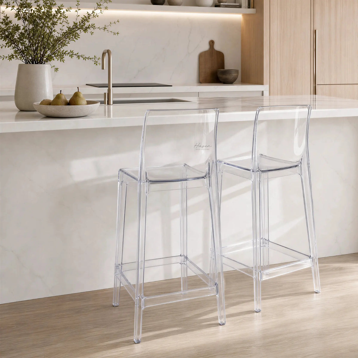 Three transparent Jupiter Counter Stools at a marble island in a light wood kitchen.
