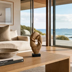 Loop Sculpture in mango wood on a black base, on a wooden console beside a beige sofa, overlooking the coast.