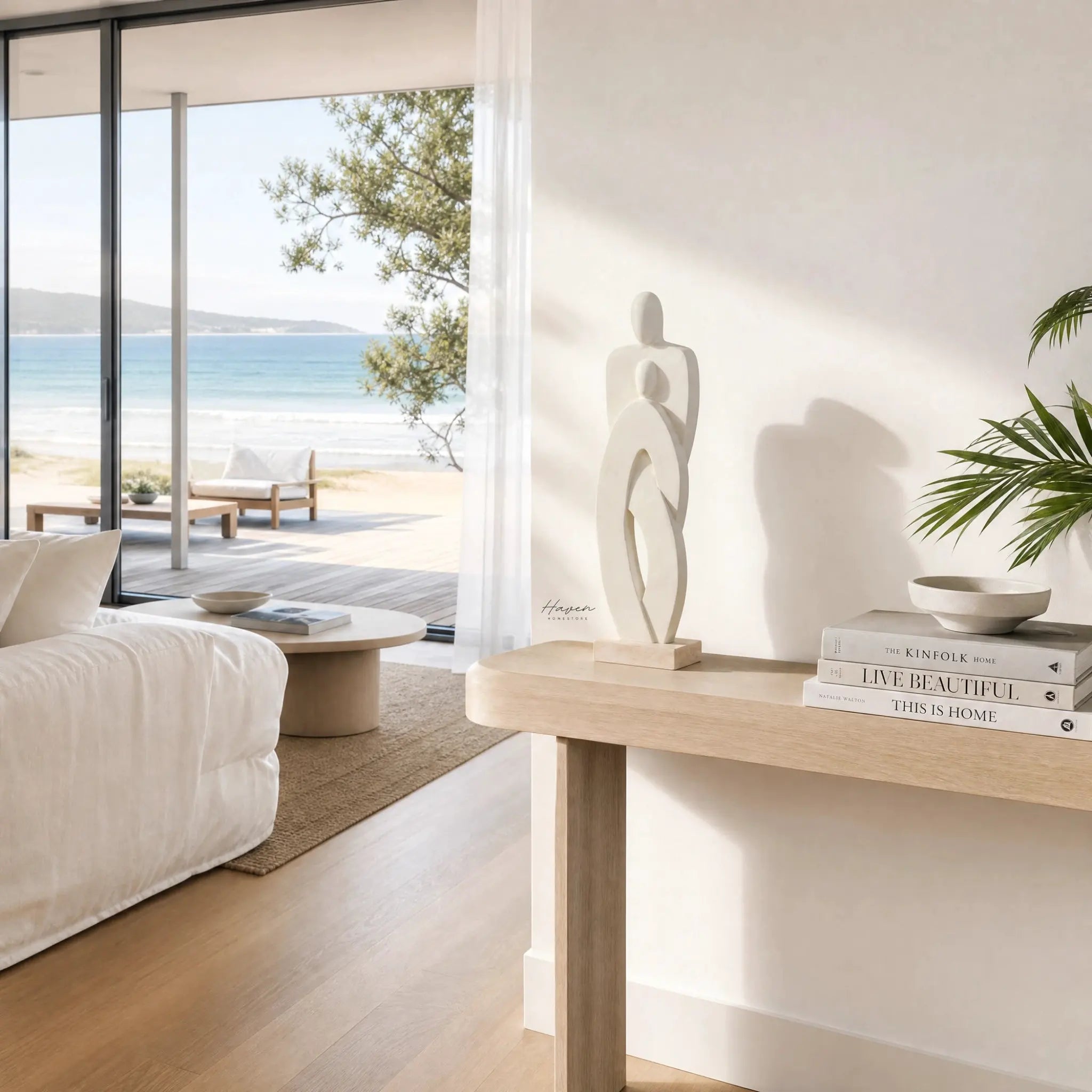 Standing Couple sculpture, mango wood, minimalist two-figure form on a living room console by a beach view.