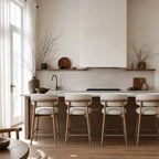 Four light ash counter stools with cream upholstery line a kitchen island, adding warmth and relaxed comfort to the space.