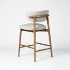 Solid ash counter stool with light beige upholstery, curved backrest, and tapered legs for relaxed kitchen seating.