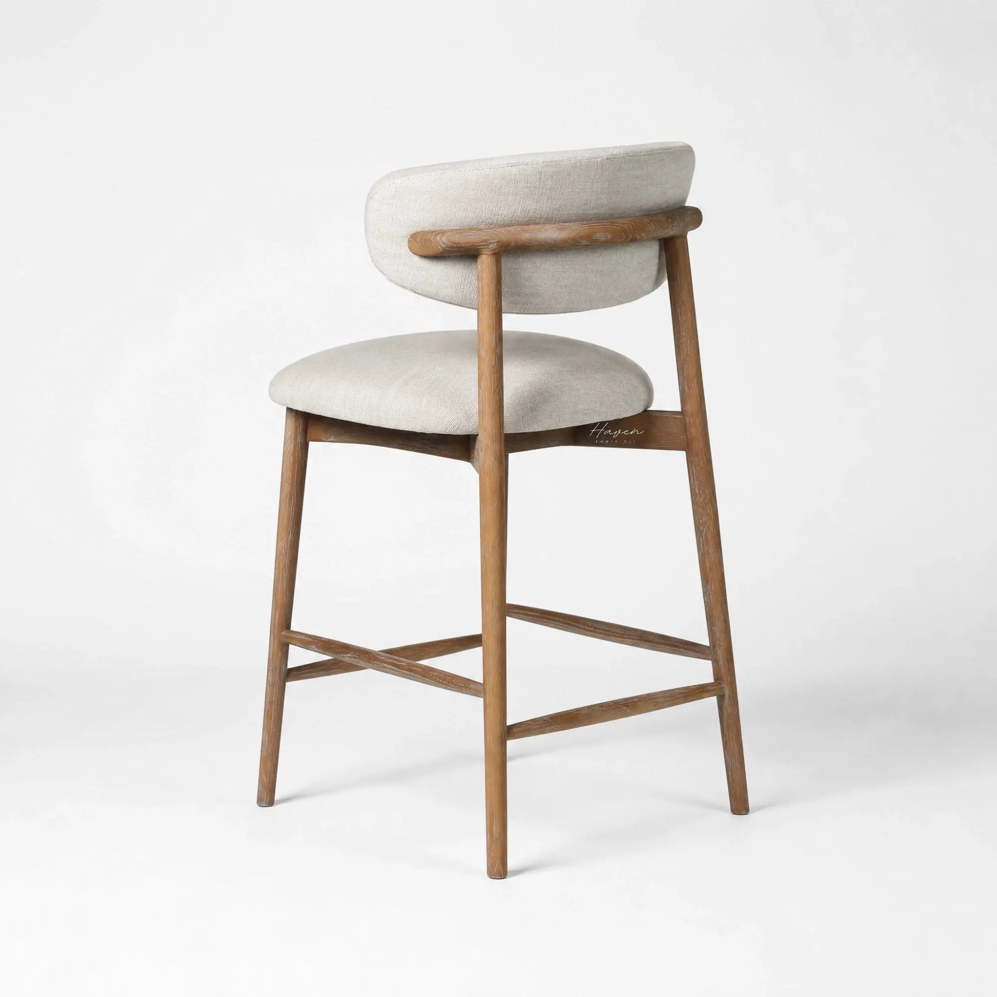 Solid ash counter stool with light beige upholstery, curved backrest, and tapered legs for relaxed kitchen seating.