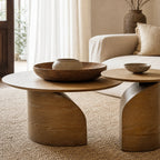 Sculptural ash coffee table duo with slim circular tops and sweeping curved pedestal bases bringing natural warmth to a living space.