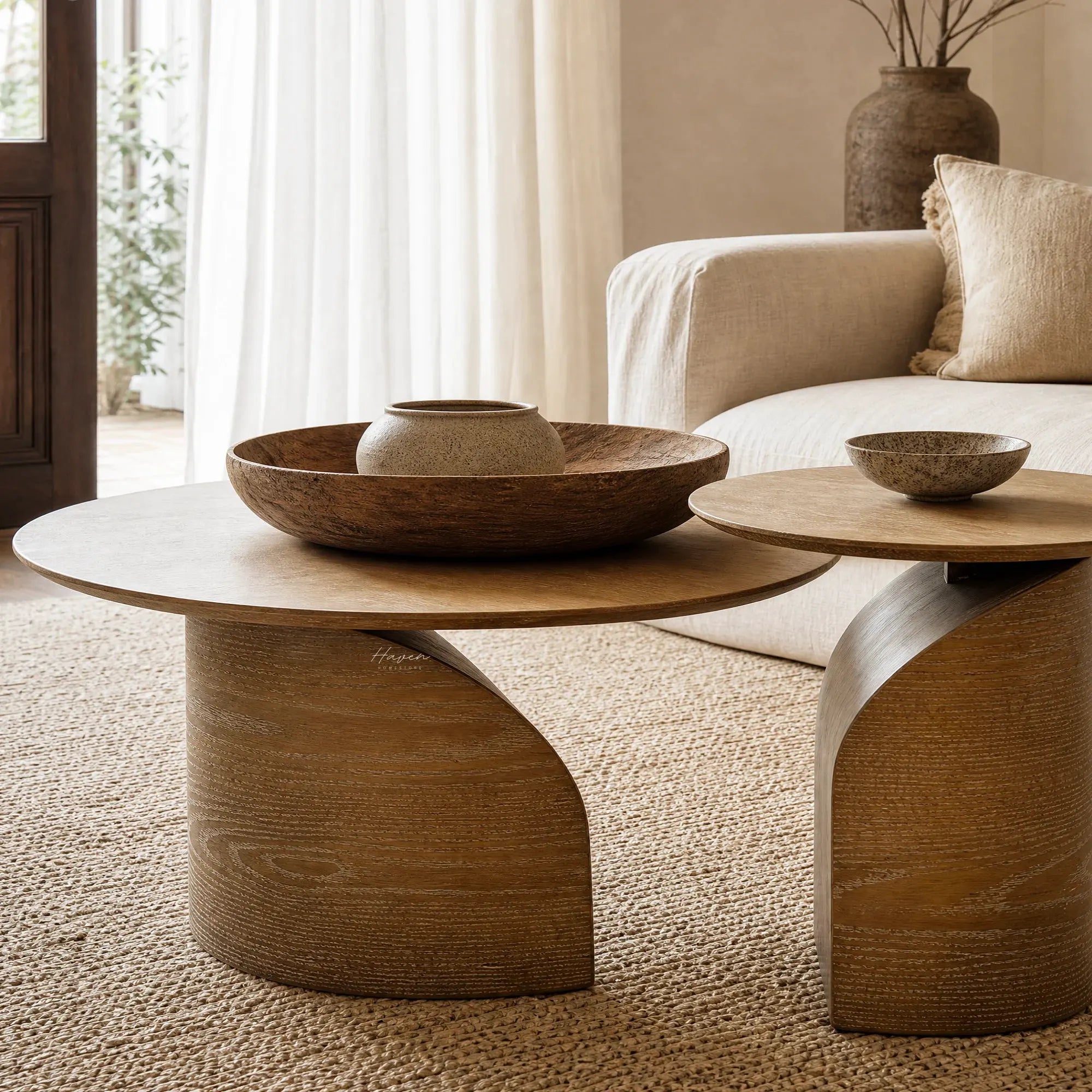 Sculptural ash coffee table duo with slim circular tops and sweeping curved pedestal bases bringing natural warmth to a living space.