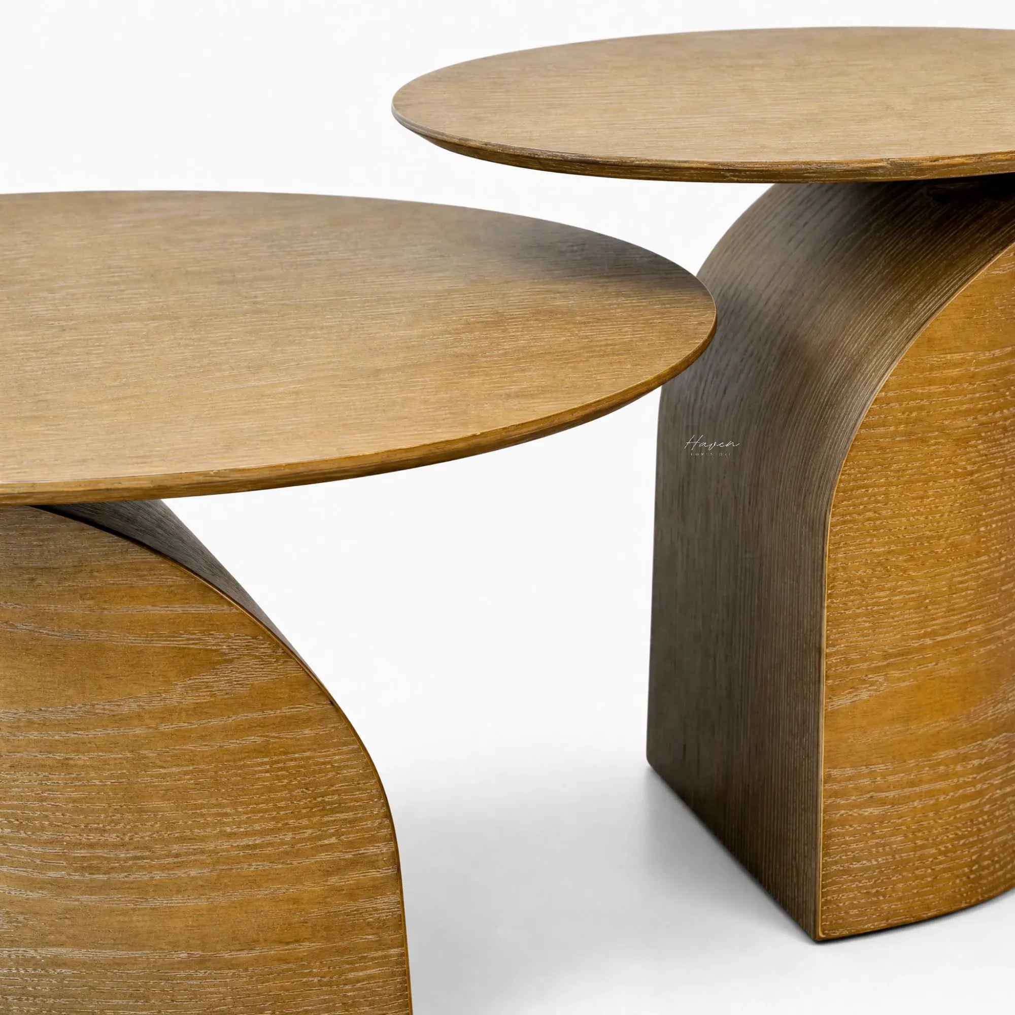 Sculptural ash coffee table duo featuring slim circular tops and sweeping curved pedestal bases with natural wood grain warmth.