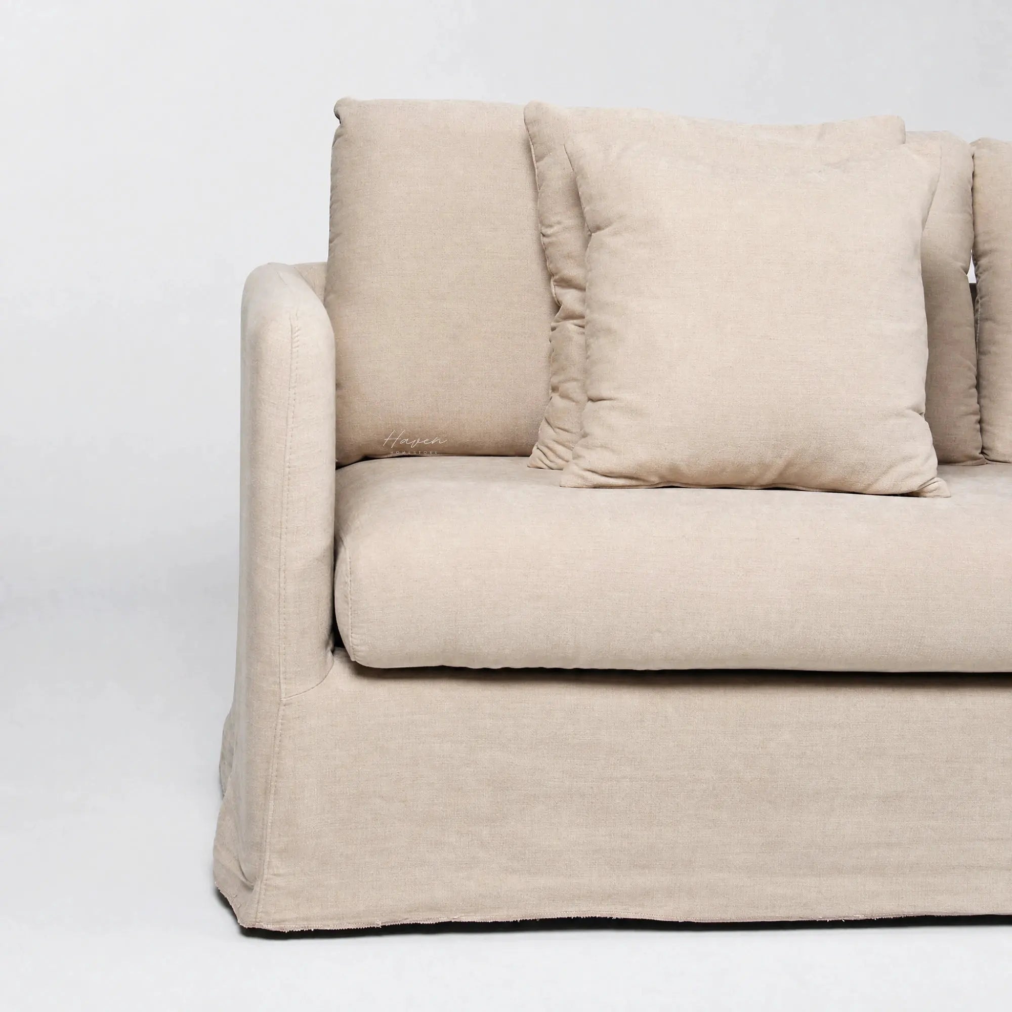 Beige slipcover sofa with soft tailored polyester fabric, generous cushioning, and a relaxed, inviting design featuring a matching throw pillow.