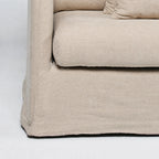 Close-up of the beige Lumi Slipcover Sofa showcasing its soft polyester texture, generous cushioning, and casually tailored skirt.