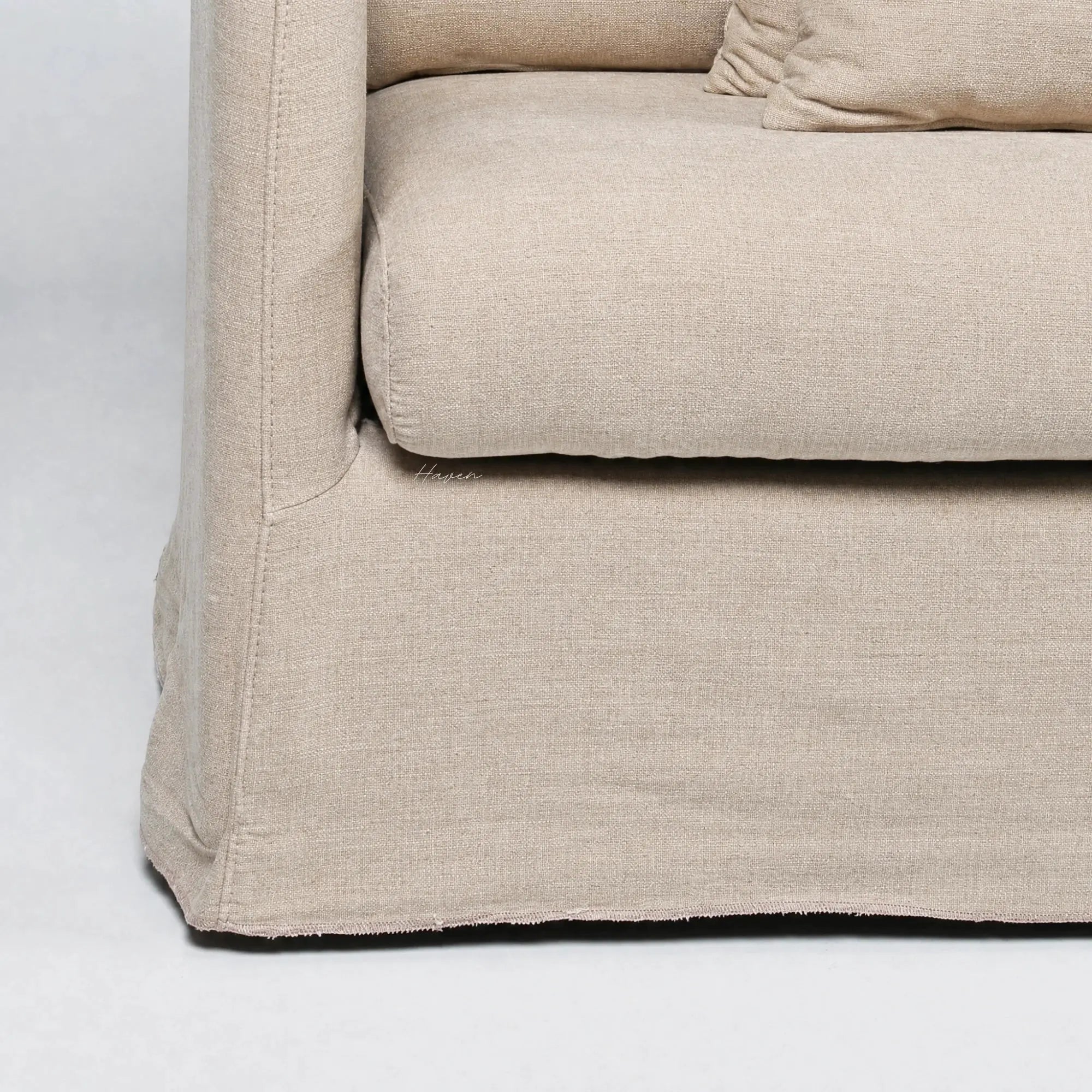 Close-up of the beige Lumi Slipcover Sofa showcasing its soft polyester texture, generous cushioning, and casually tailored skirt.